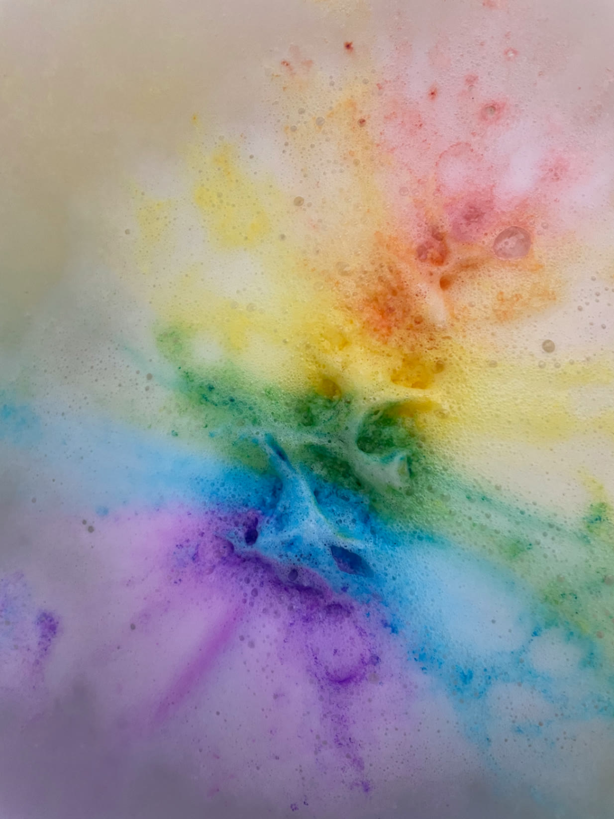 Rainbow-coloured bath foam swirling across the surface of the water